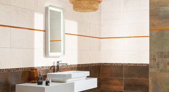 RAKO | Koupelna z obkladů v imitaci kovu v hnědé, měděné a béžové barvě. Doplněno oranžovou a tmavě hnědou dekorovanou listelou.