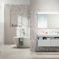 RAKO | Koupelna z obkladů s imitací teraco v odstínu světle šedé v kombinaci s šedou falešnou mozaikou. Na podlaze dlažba v odstínu slonové kosti.