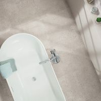 RAKO | Pohled shora na podlahu v koupelně, která je vytvořená z dlažby s imitací teraco ve světle šedé barvě.