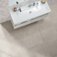 RAKO | Pohled shora na dlažbu s imitací teraco ve světle šedé barvě a obklad s dekorem falešné mozaiky v šedé barvě.