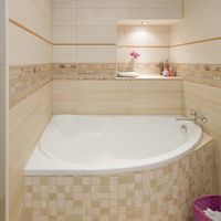 RAKO | Koupelna v béžové a světle béžové imitaci s jemným dřevem. Doplněno o květinový dekor a oranžovou listelu.