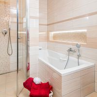 RAKO | Koupelna z lesklých obkladů v odstínech béžové barvy s imitací travertinu a jemným žilkováním. Doplněno o listelu a mozaiku.