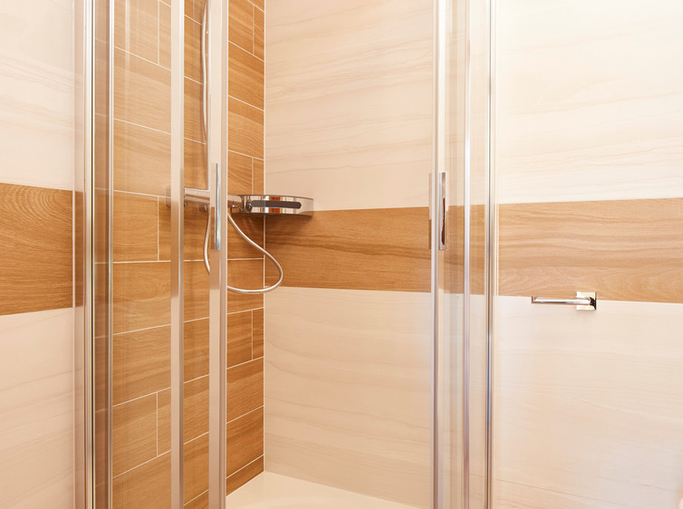 RAKO | Koupelna v bílé barvě s imitací mramoru. Doplněna o dlažbu s imitací dřeva v hnědé barvě.