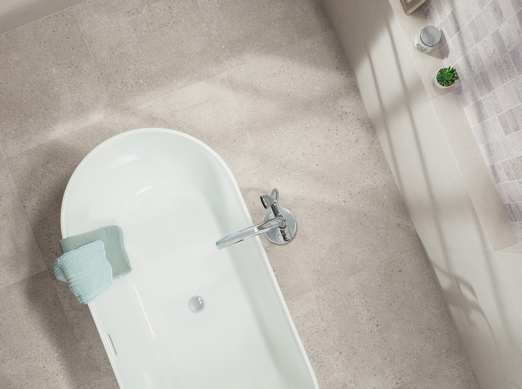 RAKO | Pohled shora na podlahu v koupelně, která je vytvořená z dlažby s imitací teraco ve světle šedé barvě.