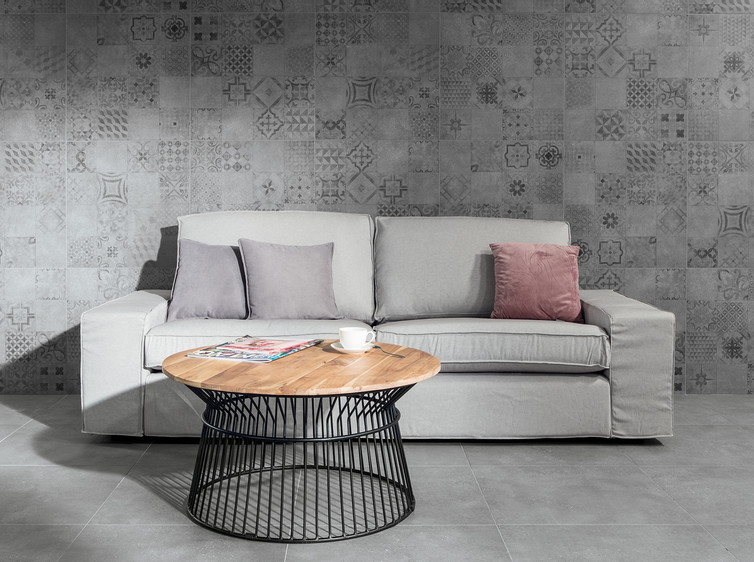 RAKO | Obývací pokoj vytvořený z dlažby s imitací industriálního betonu v šedé barvě. Zeď obložená toutéž dlažbou s patchworkovým motivem. 