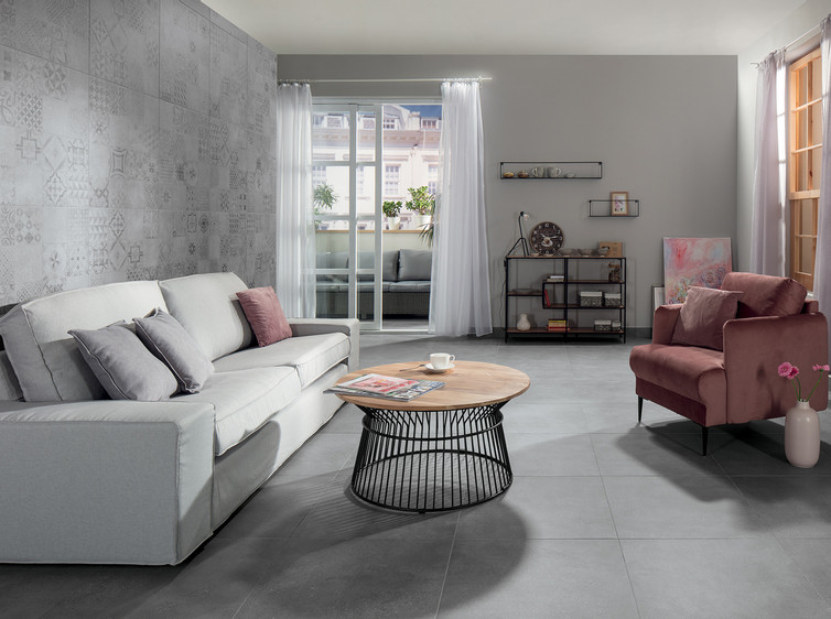 RAKO | Obývací pokoj vytvořený z dlažby s imitací industriálního betonu v šedé barvě. Zeď obložená toutéž dlažbou s patchworkovým motivem. 