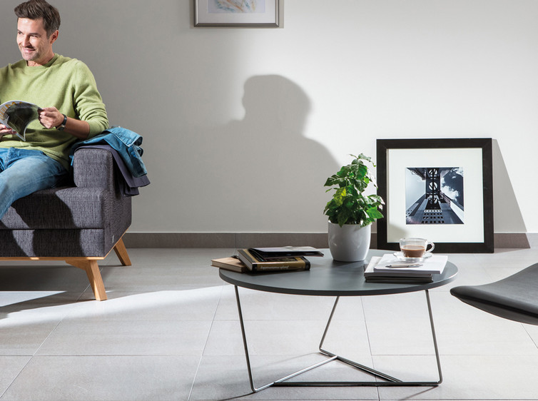 RAKO | Velkoformátová dlažba v šedé barvě s imitací kamene, využitá v obývacím pokoji.