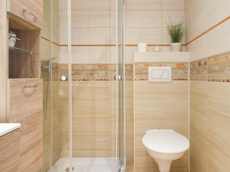 RAKO | Koupelna v béžové a světle béžové imitaci s jemným dřevem. Doplněno o květinový dekor a oranžovou listelu.